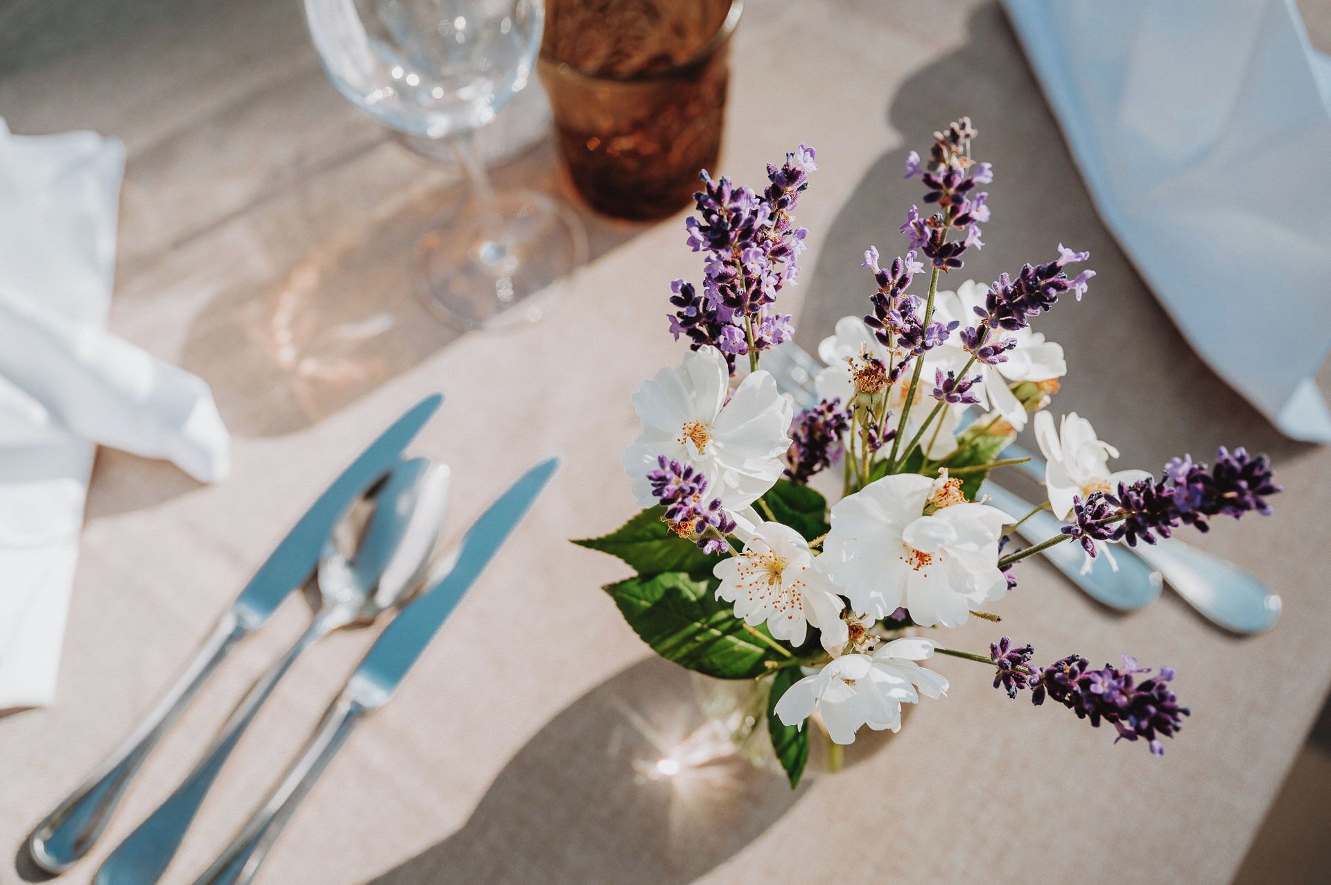 A table setting with a vase of white and purple flowers, a glass of water, and cutlery.