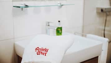 Un baño con un lavamanos blanco, un estante de vidrio arriba y una toalla con texto rojo.