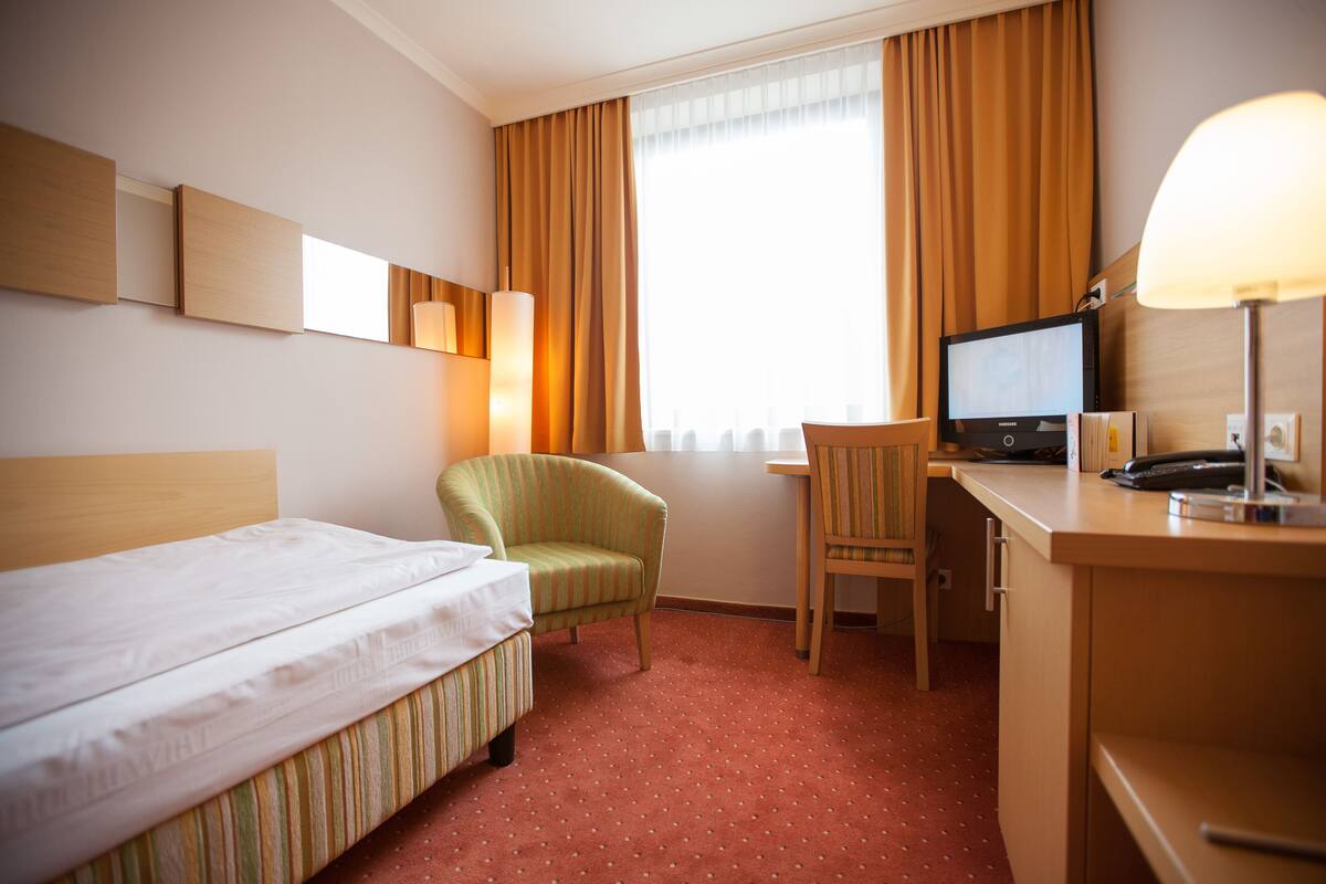 Ein Hotelzimmer mit einem Bett, einem Schreibtisch mit Computer, einem Sessel und einer Lampe.