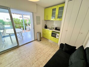 A compact kitchen with a sliding glass door leading to an outdoor patio, a small trash bin, and a black sofa in the living area.