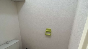 A small bathroom with a toilet, a green seat, and a white bucket.