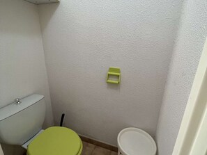 A small bathroom with a toilet, a green seat, and a white bucket.