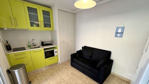 A compact living space with a kitchenette, a black sofa, and a trash bin.