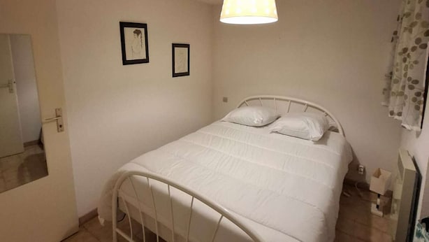 A small, neatly arranged bedroom with a single bed, a hanging light fixture, and two framed pictures on the wall.