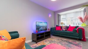 A living room with a green sofa, a flat-screen TV, and a colorful rug.