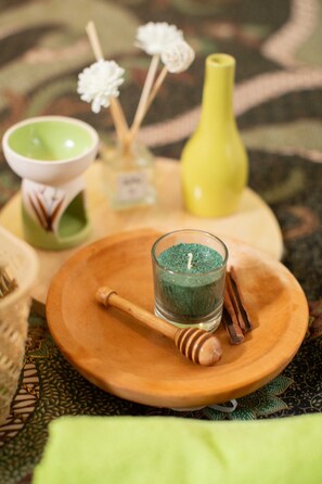 A wooden table with a glass candle holder, a honey dipper, and a small green candle. - 1O1 Urban Jakarta Pemuda (Jakarta)