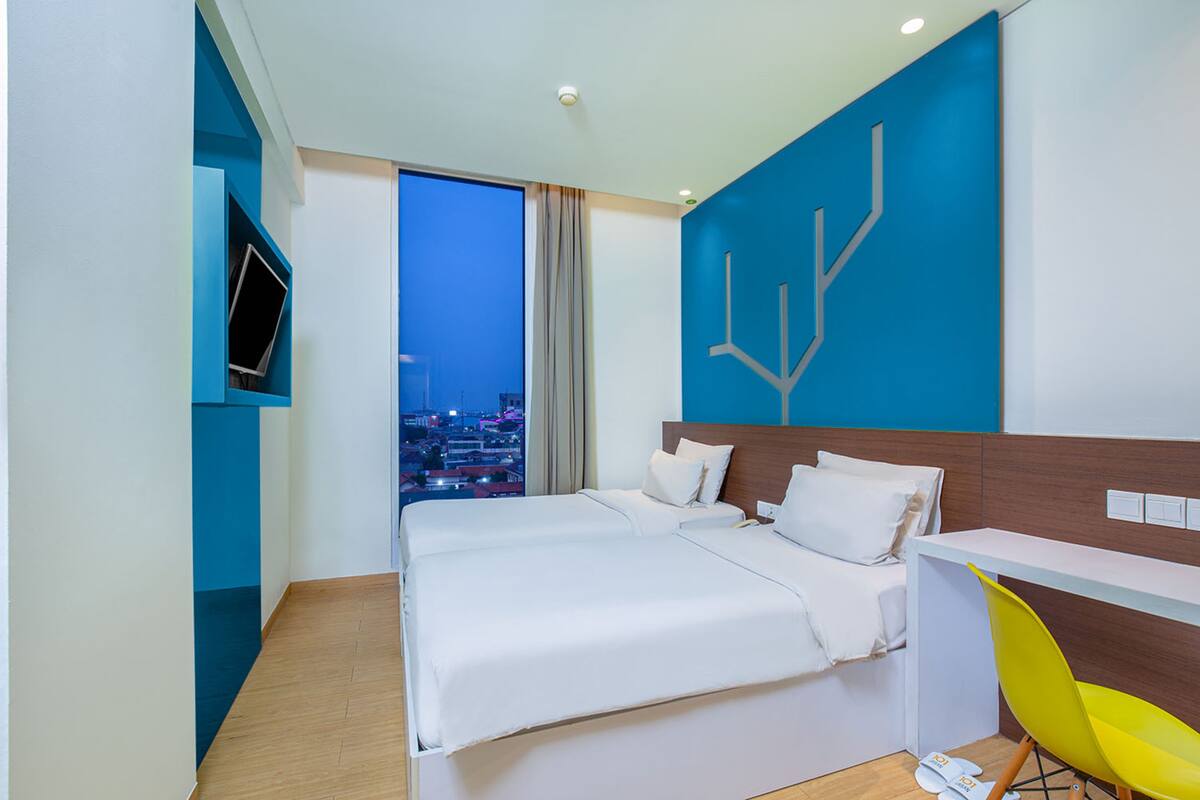 A modern hotel room with a large bed, a desk, and a view of the city at night.