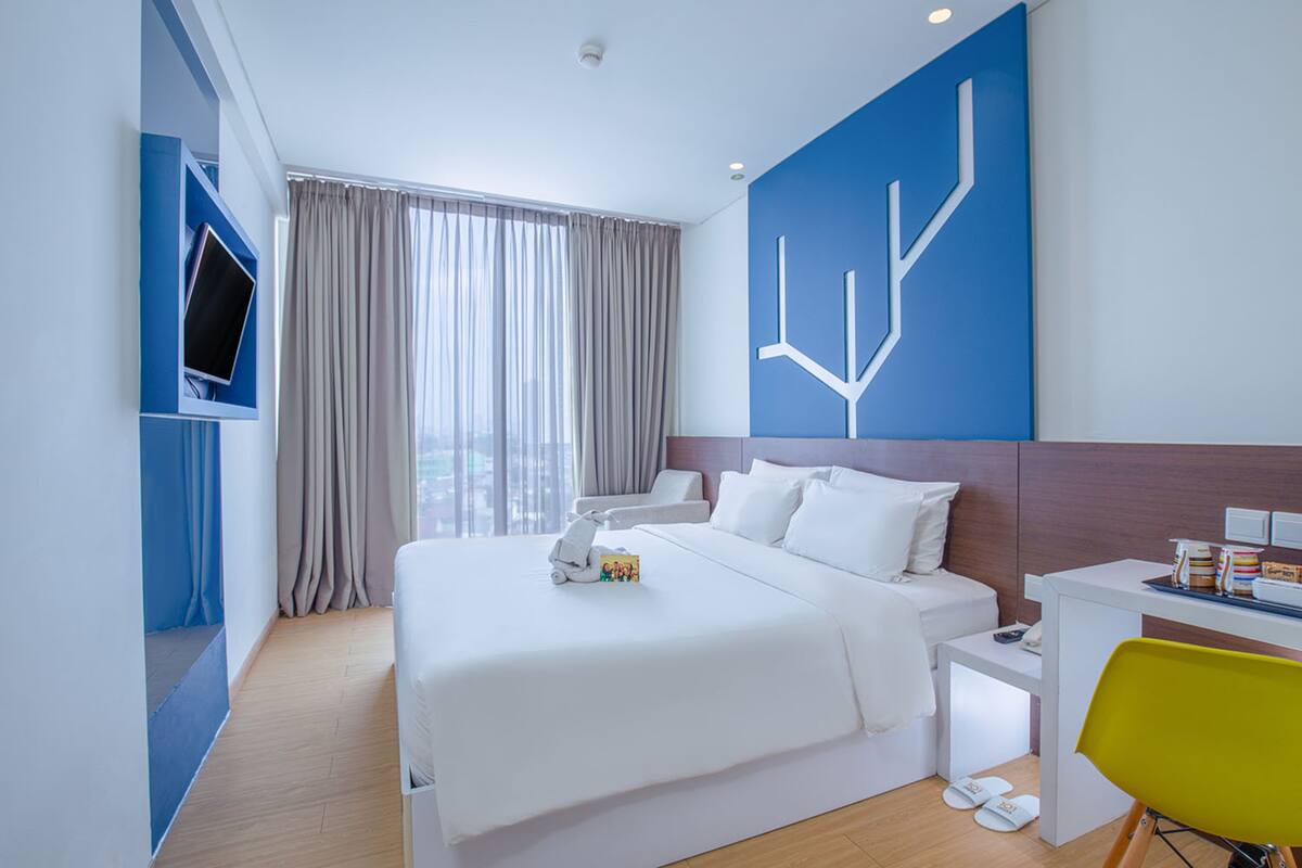 A modern hotel room with a large bed, a desk, and a TV mounted on the wall.