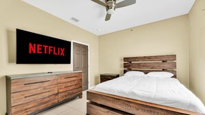 A bedroom with a wooden bed, a wooden dresser, a TV mounted on the wall, and a ceiling fan. - Relax & Enjoy In Our Spacious Townhome Getaway! (McAllen)