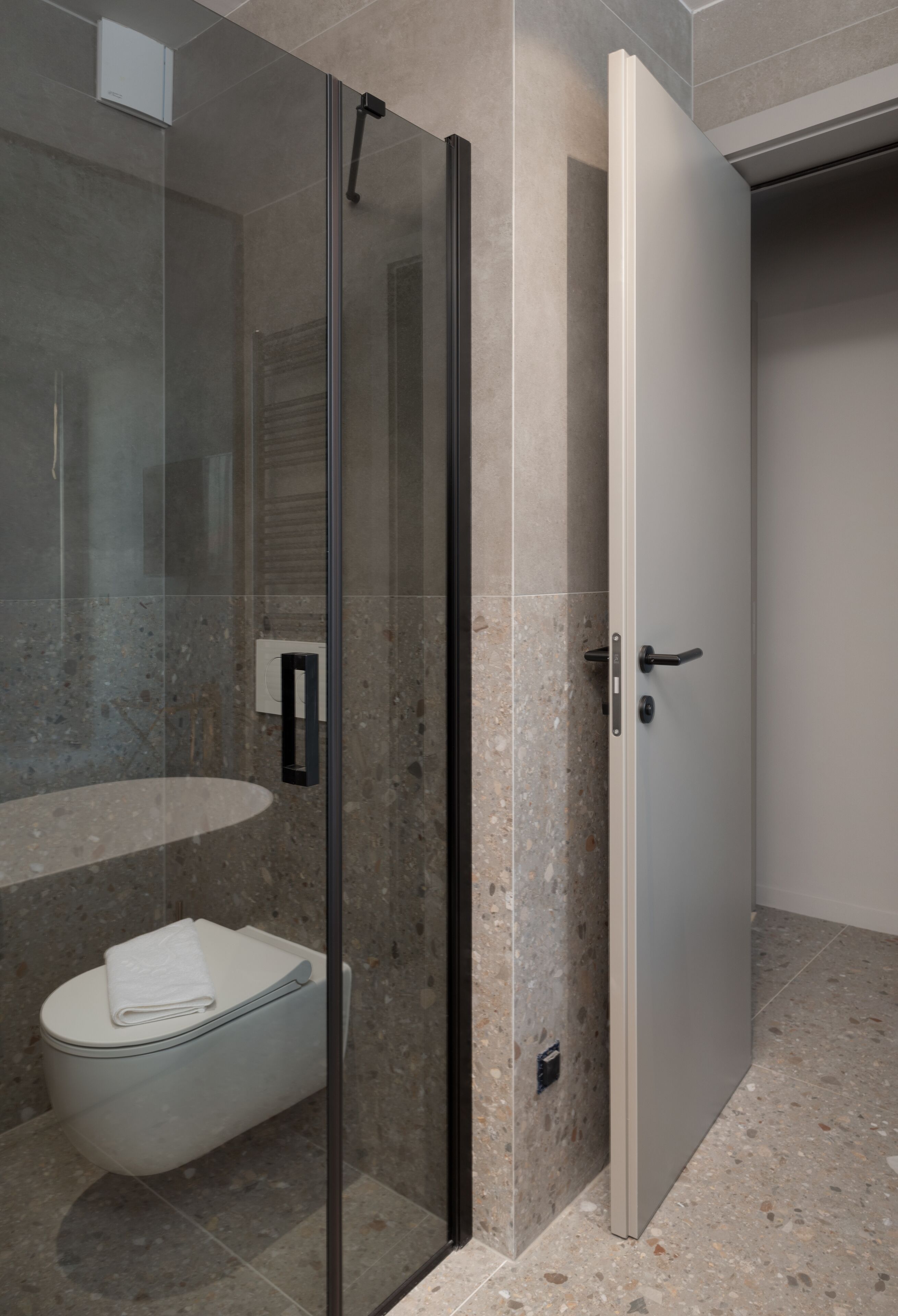 Ein modernes Badezimmer mit einer Glaskabine zur Dusche, einer weißen Toilette und einem marmorverlegten Boden.
