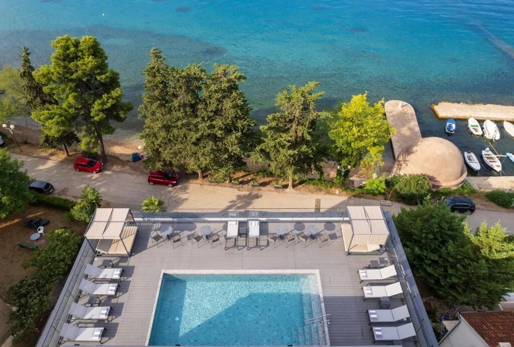 Vista aerea di un resort con piscina, spiaggia e imbarcazioni.