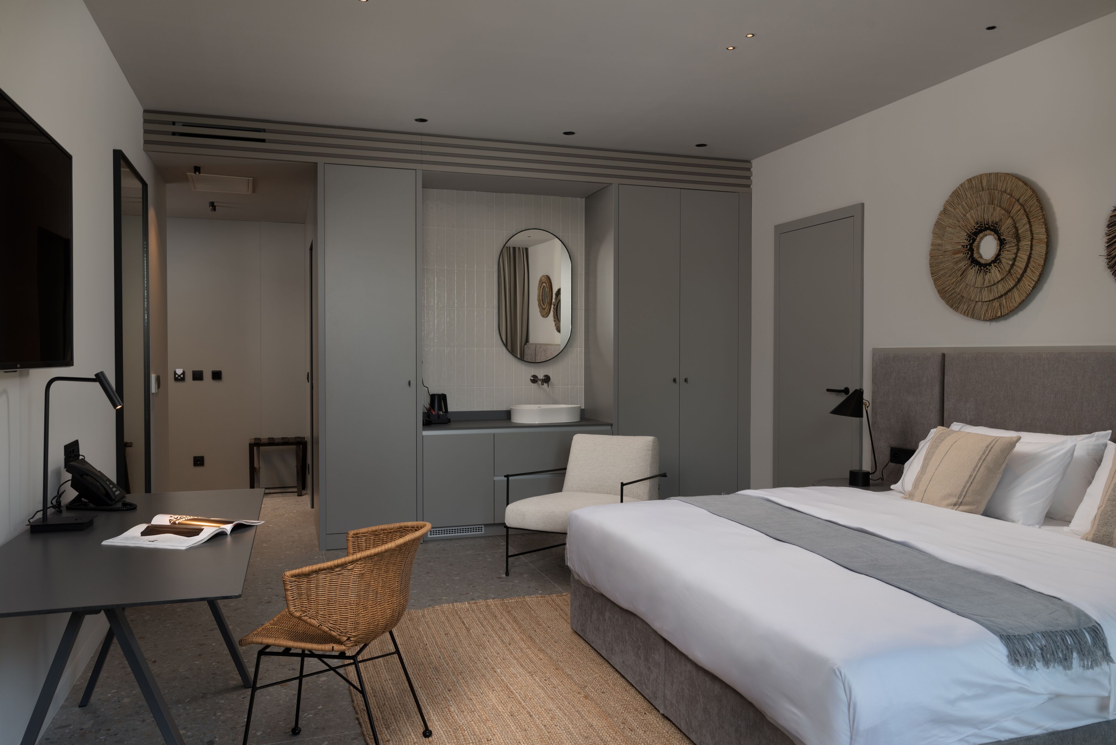 Una camera d'albergo moderna con un letto grande, una scrivania, una sedia e un bagno con uno specchio e un lavandino.