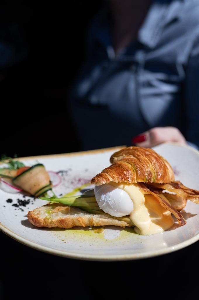 Un plato con un croissant, huevo y salsa, acompañado de una guarnición de vegetales.