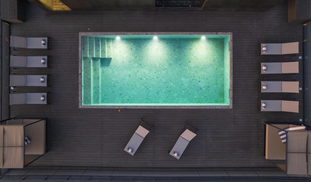A rooftop pool with a rectangular shape, surrounded by lounge chairs and a wooden deck.