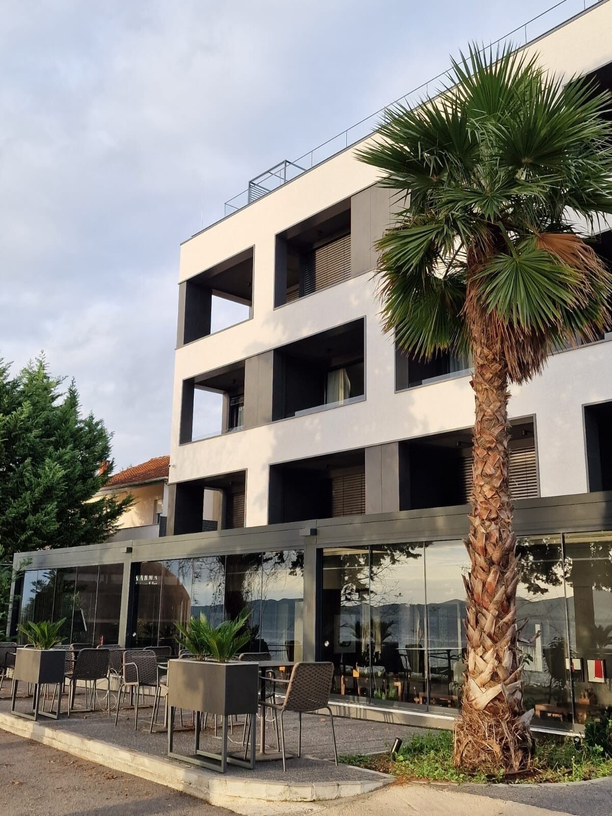 Un edificio moderno con fachada de vidrio, zona de estar al aire libre y una palmera.