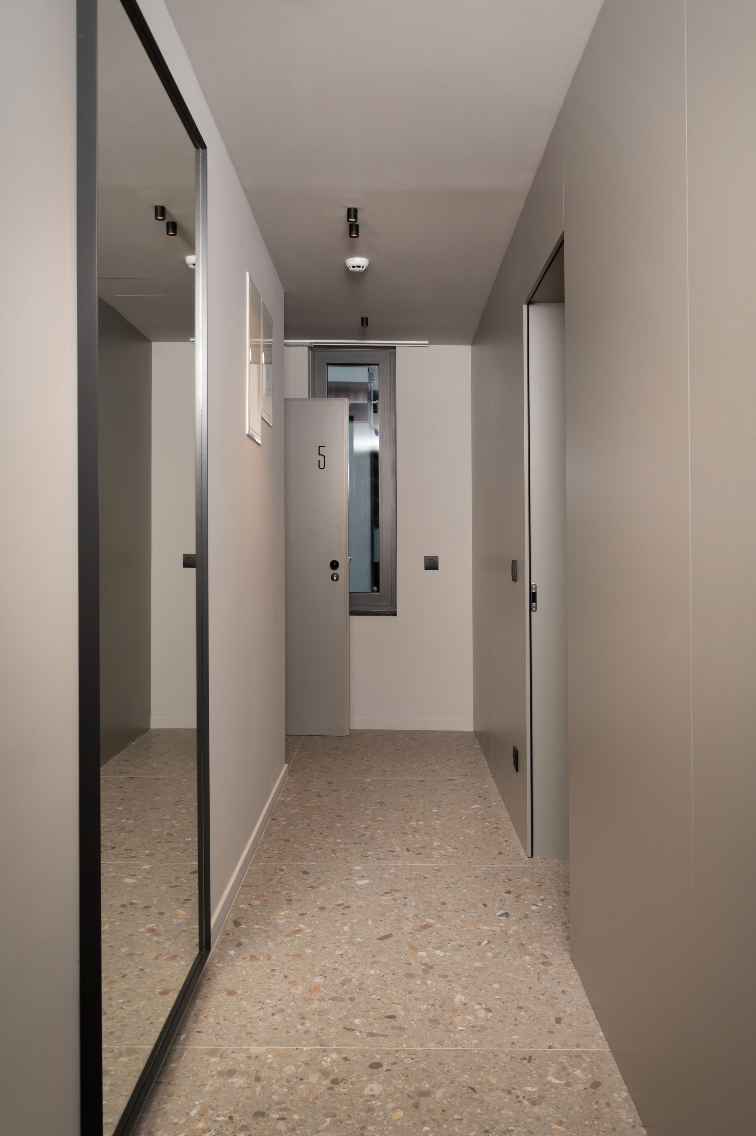Un couloir avec un mur recouvert de miroirs, une porte portant le numéro 5 et un petit ascenseur.