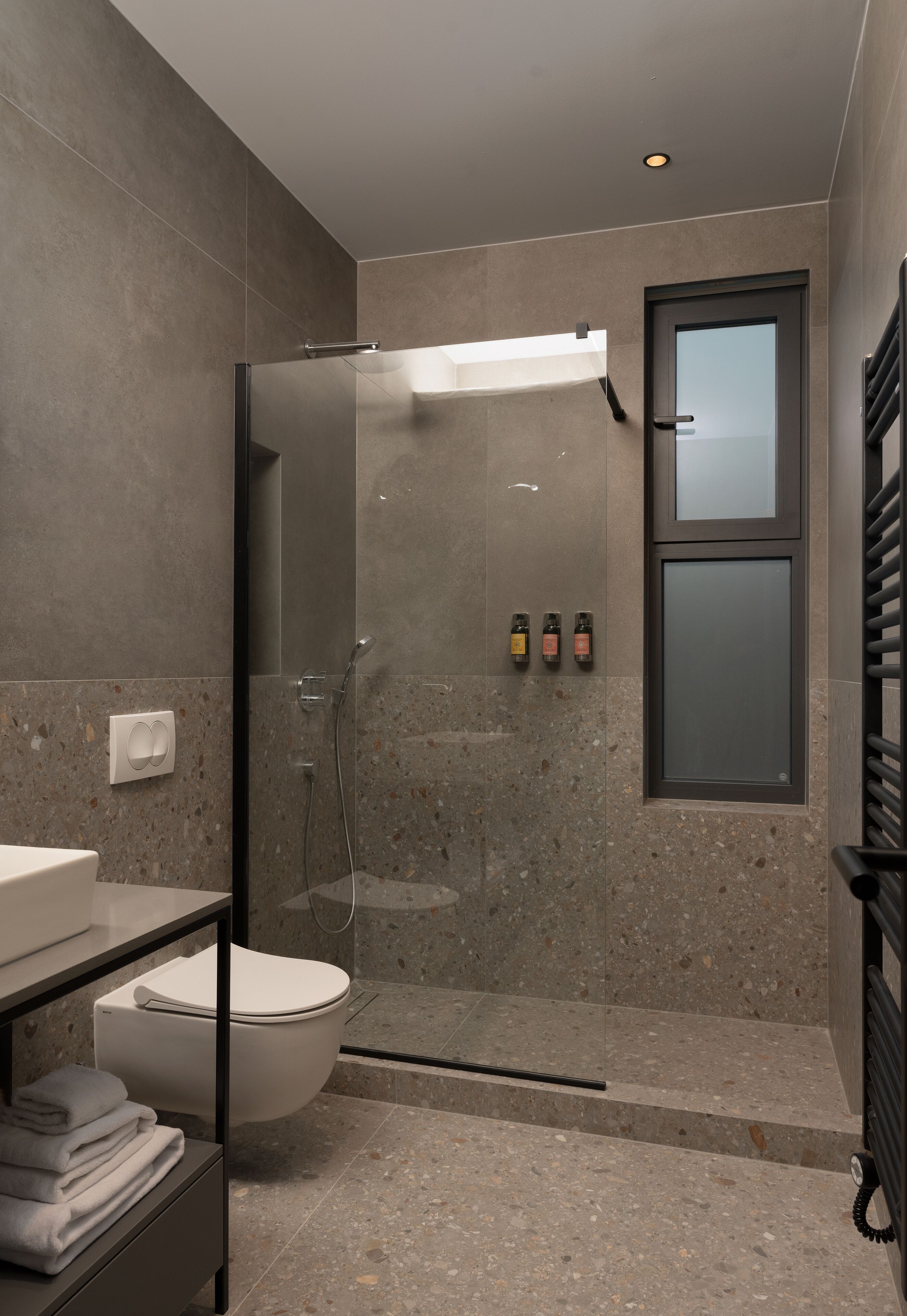 Un baño moderno con ducha de mampara de vidrio, inodoro y lavamanos con una pila de toallas.