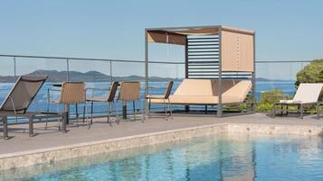 A poolside area with lounge chairs and a canopy, overlooking a body of water and distant hills.