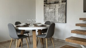 A dining area with a round table, grey upholstered chairs, and a gold pendant light.