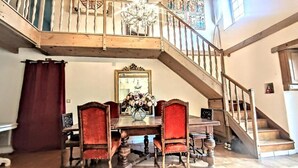 A dining area with a wooden table, red upholstered chairs, and a chandelier. A staircase leads to an upper level. - La Maison bleue (Cuncy-lès-Varzy)