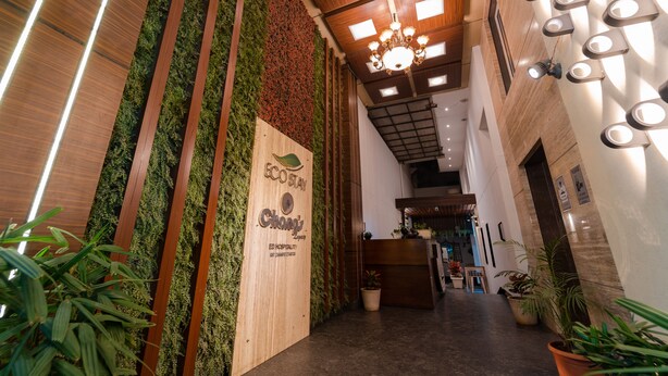 Un espace d’accueil d’hôtel avec un comptoir de réception en bois, un jardin vertical verdoyant et un lustre.