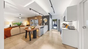 Une cuisine moderne avec un îlot central, un coin repas doté d’une table en bois et un salon avec un canapé et un tableau.
