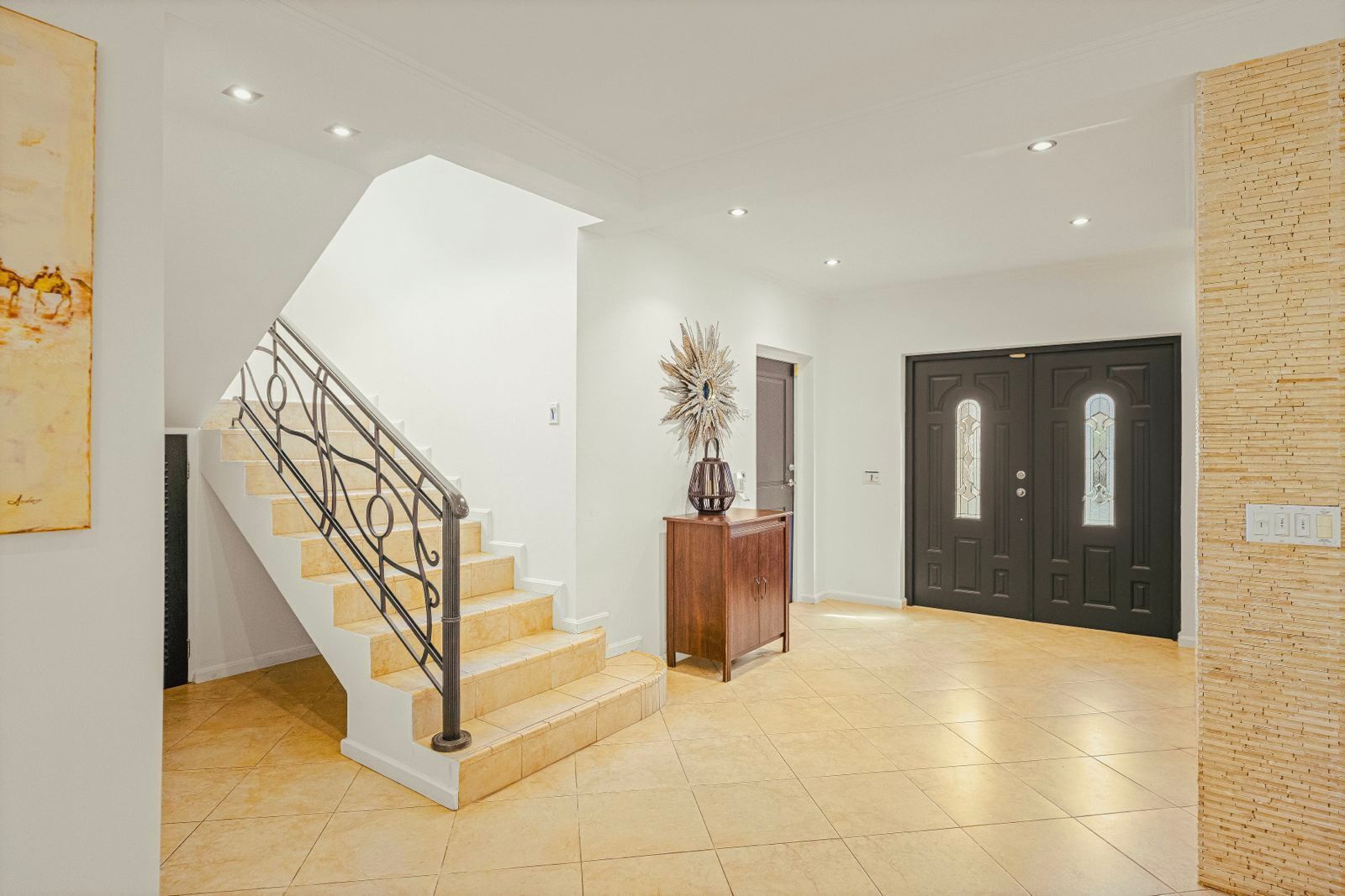 A spacious foyer with a staircase, a dark wooden door, and a decorative vase on a pedestal.