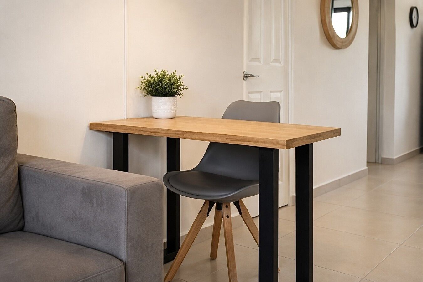 Un espace de repas moderne avec une table en bois, une chaise noire, un canapé gris et une plante en pot.