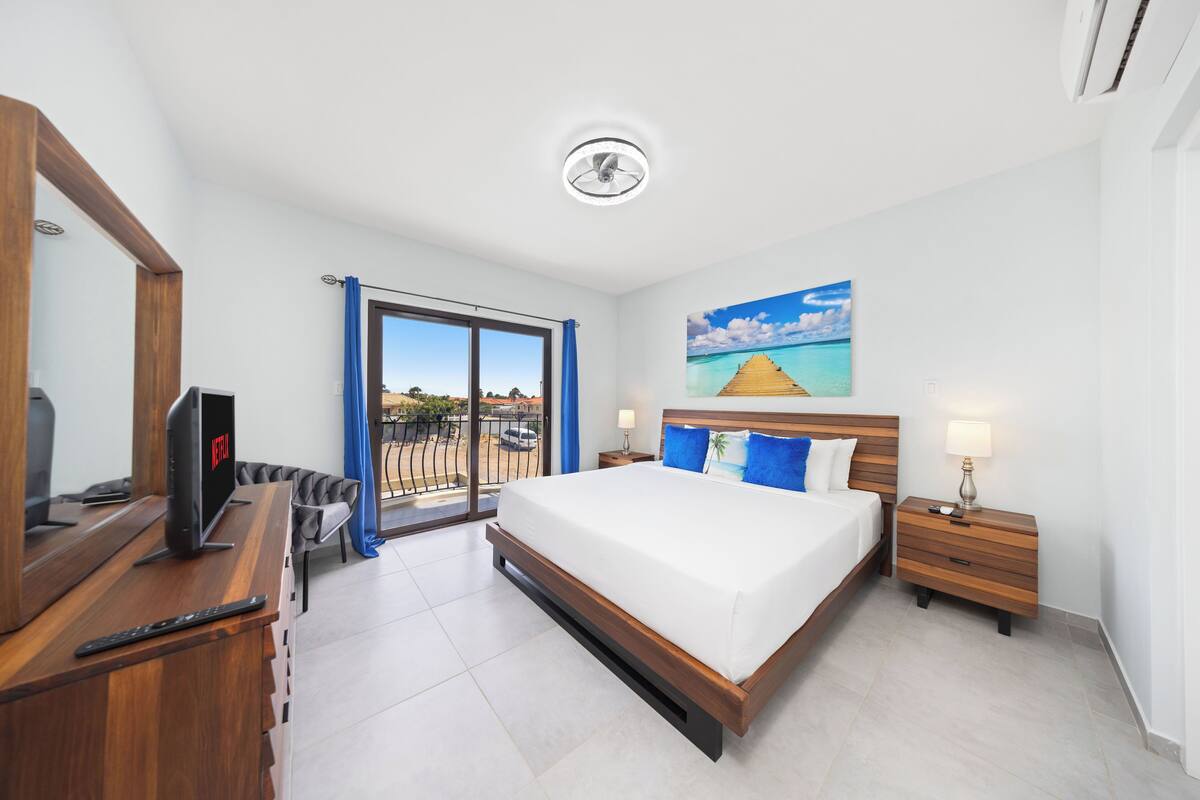 Ein Hotelzimmer mit einem großen Bett, einem Fernseher, einem Schreibtisch und einem Balkon mit Blick.