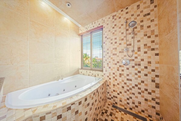 Un baño con una bañera independiente, ducha con cabezal de ducha manual y una ventana con persianas.