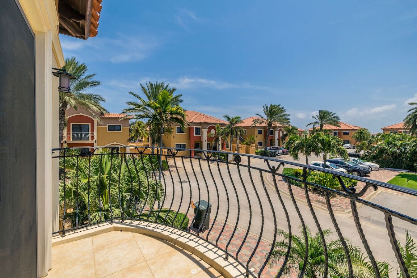 A residential area with houses, palm trees, and a curved balcony with a metal railing.