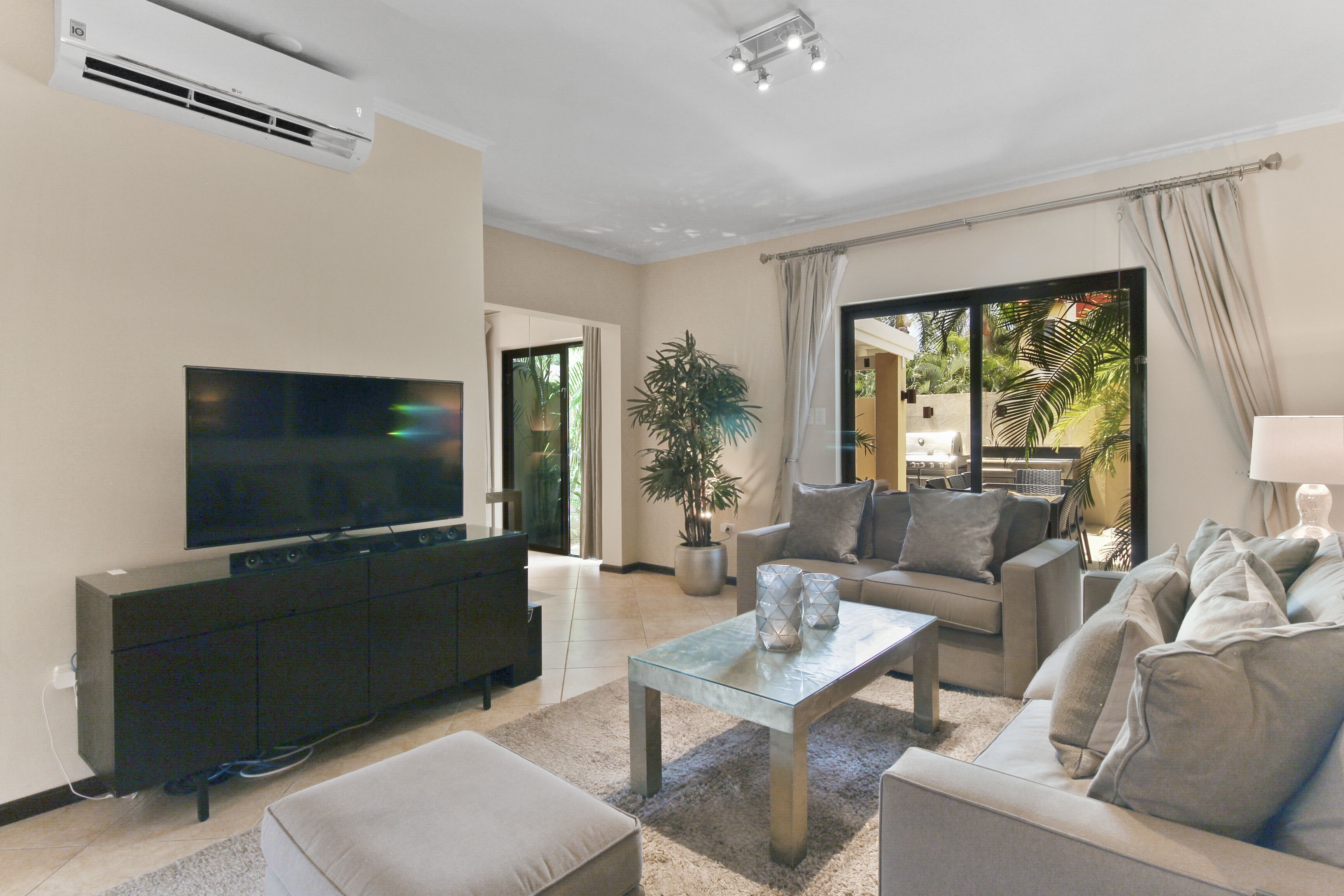 A modern living room with a flat-screen TV, a glass coffee table, and a sofa set.