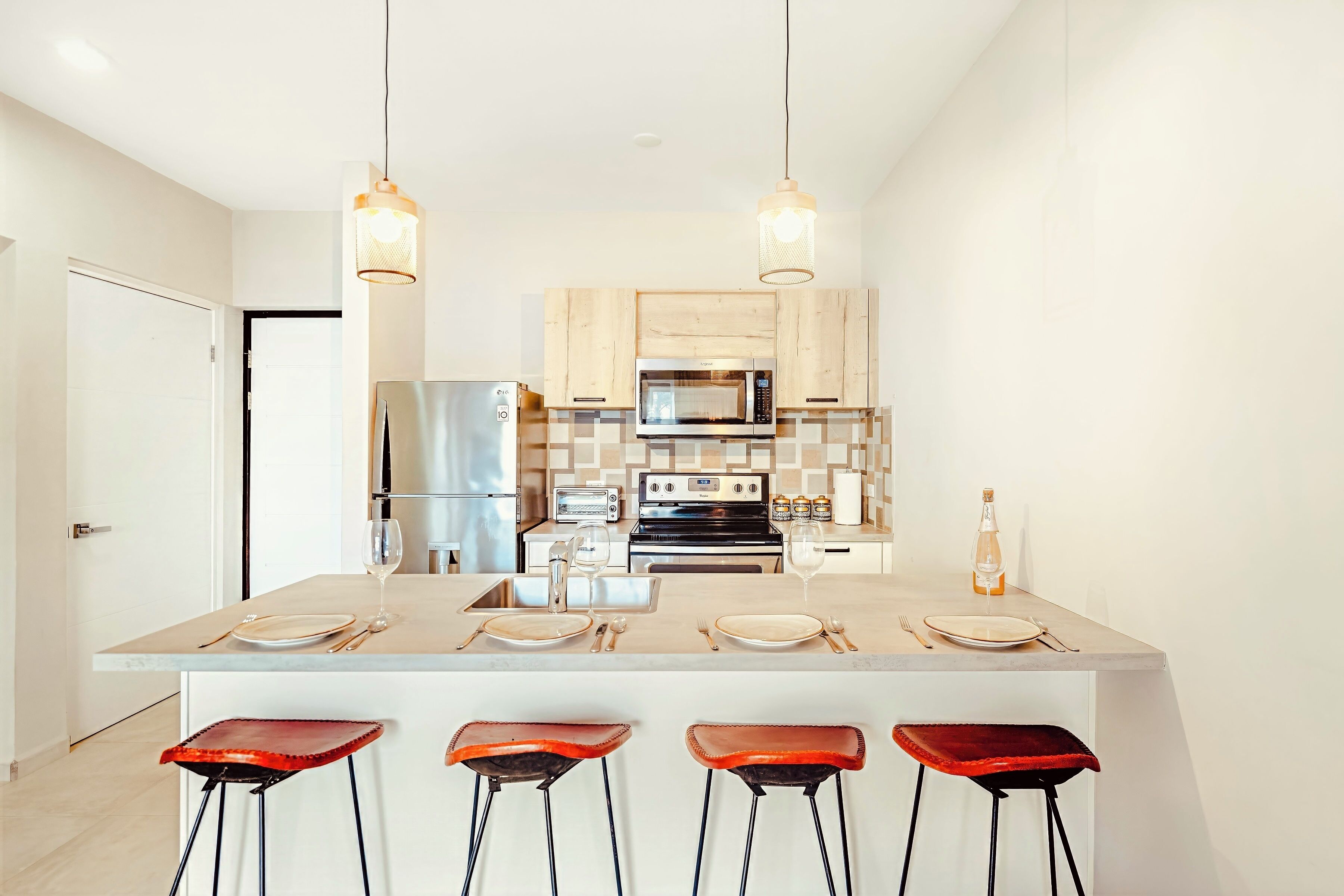 A modern kitchen with a central island, bar stools, a refrigerator, a microwave, a toaster, and hanging pendant lights.