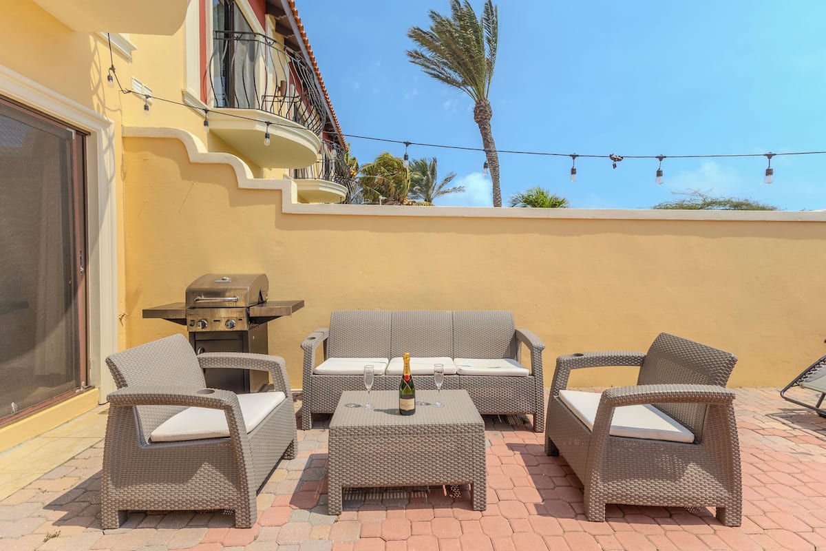 Eine Terrasse im Freien mit Korbmöbeln, einem Grill und einer Champagnerflasche.