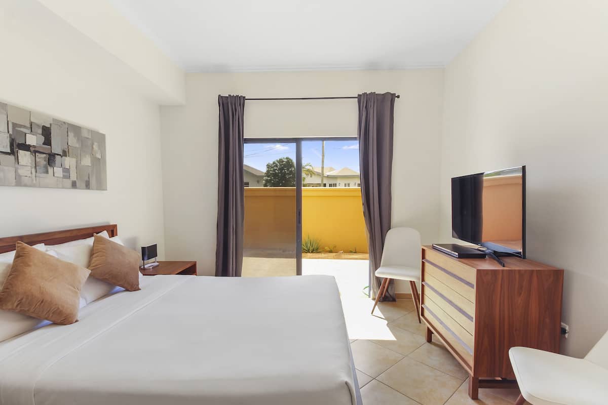 Ein Hotelzimmer mit Bett, Fernseher auf einem Holzschrank, einem Sessel und Blick ins Freie.