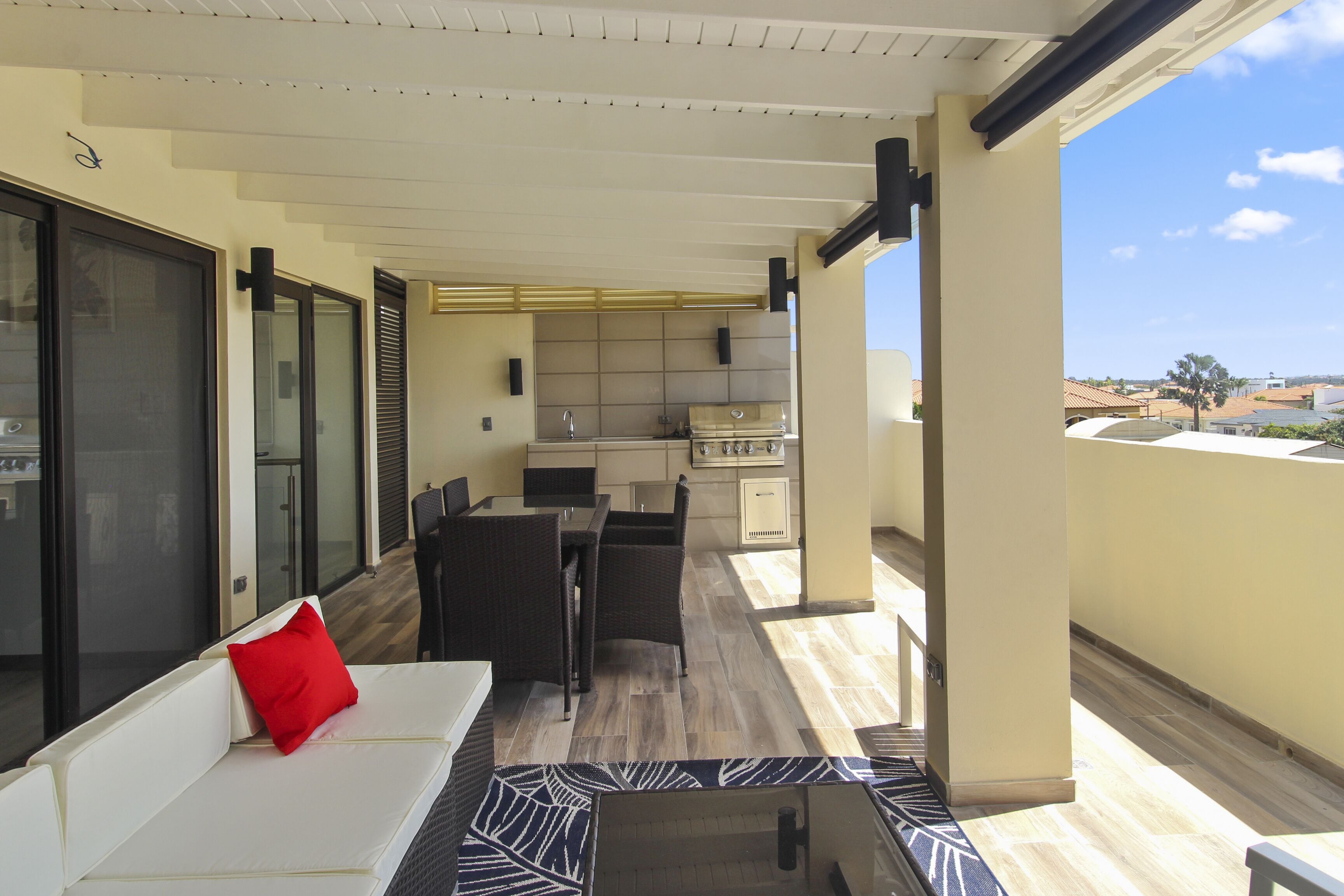 A balcony with a sofa, a dining table, and chairs. There is a kitchen area with cabinets and a countertop.