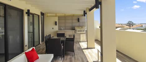 A balcony with a sofa, a dining table, and chairs. There is a kitchen area with cabinets and a countertop.