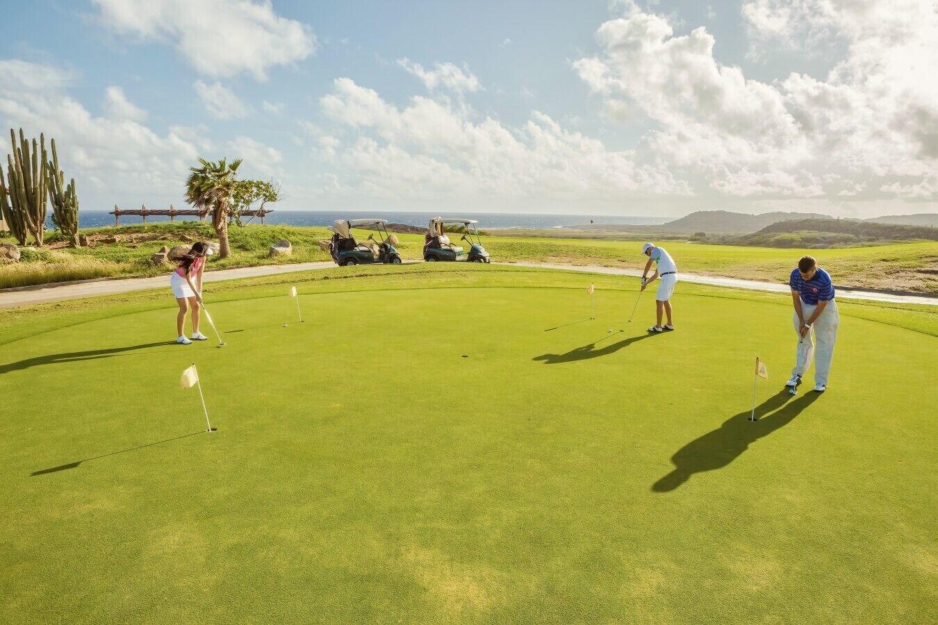 Um campo de golfe com jogadores, céu limpo e montanhas ao longe.