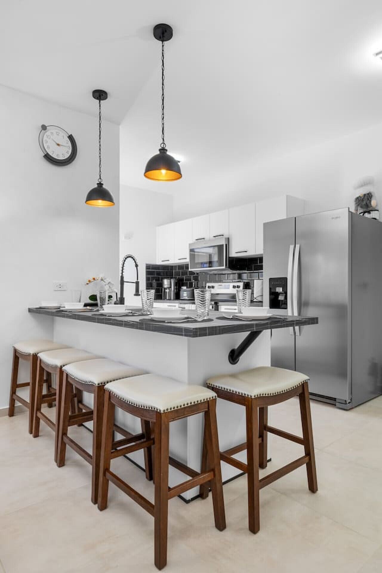 A modern kitchen with a central island, bar stools, stainless steel appliances, and pendant lighting.