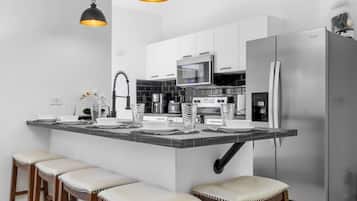 A modern kitchen with a central island, bar stools, stainless steel appliances, and pendant lighting.