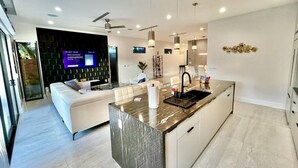 Una cocina moderna con una isla de mármol, armarios blancos e iluminación colgante.