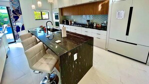 Una cocina moderna con una isla central, muebles blancos e iluminación colgante.