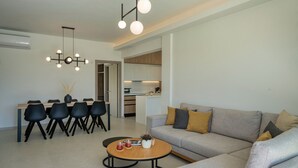 Uma sala de estar moderna com um sofá cinzento, cadeiras pretas, uma mesa de centro de madeira e uma área de jantar com mesa e cadeiras.