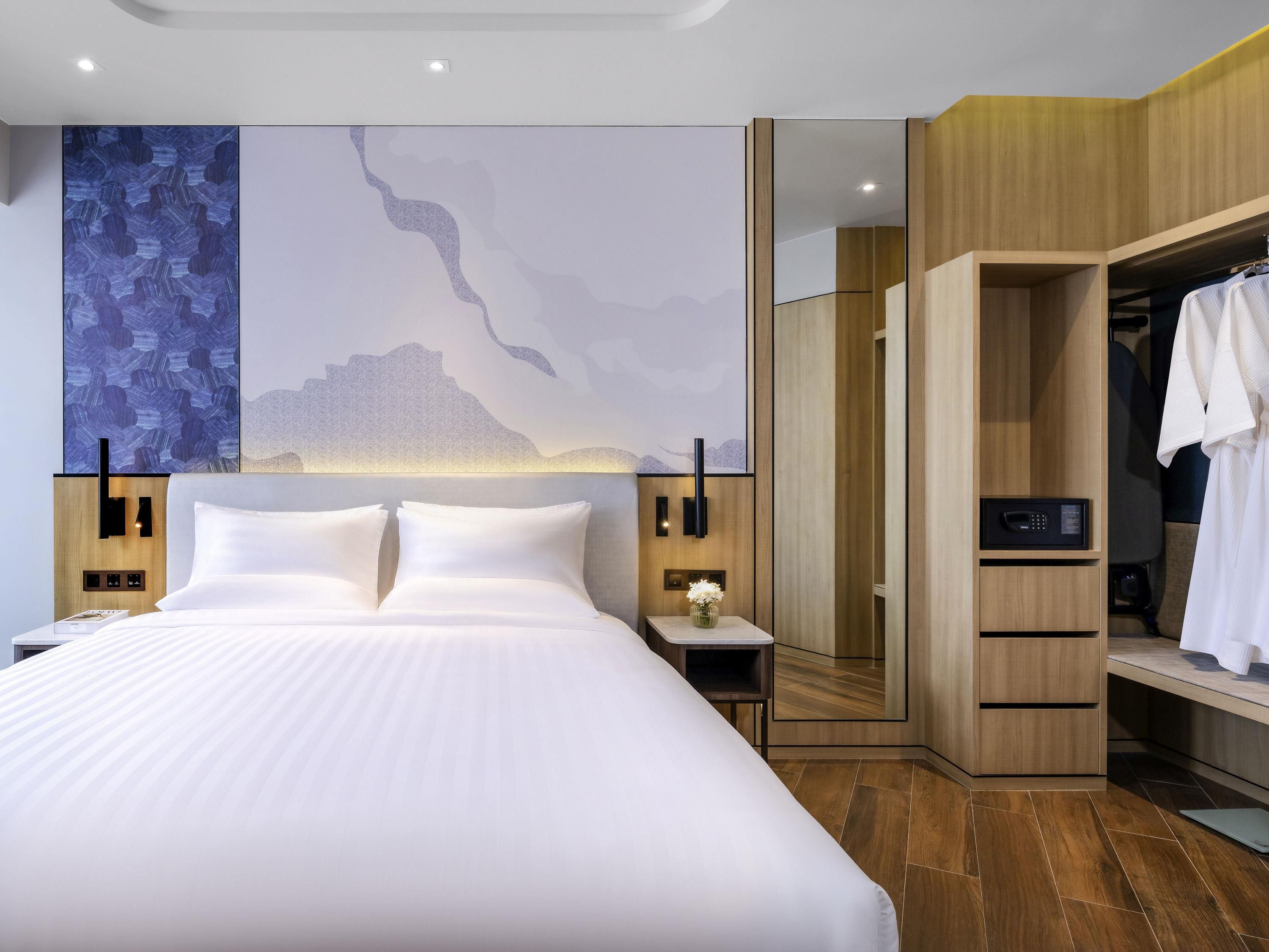 Ein modernes Hotelzimmer mit einem großen Bett, einem Holzschrank und einer Wand mit abstrakter Kunst.