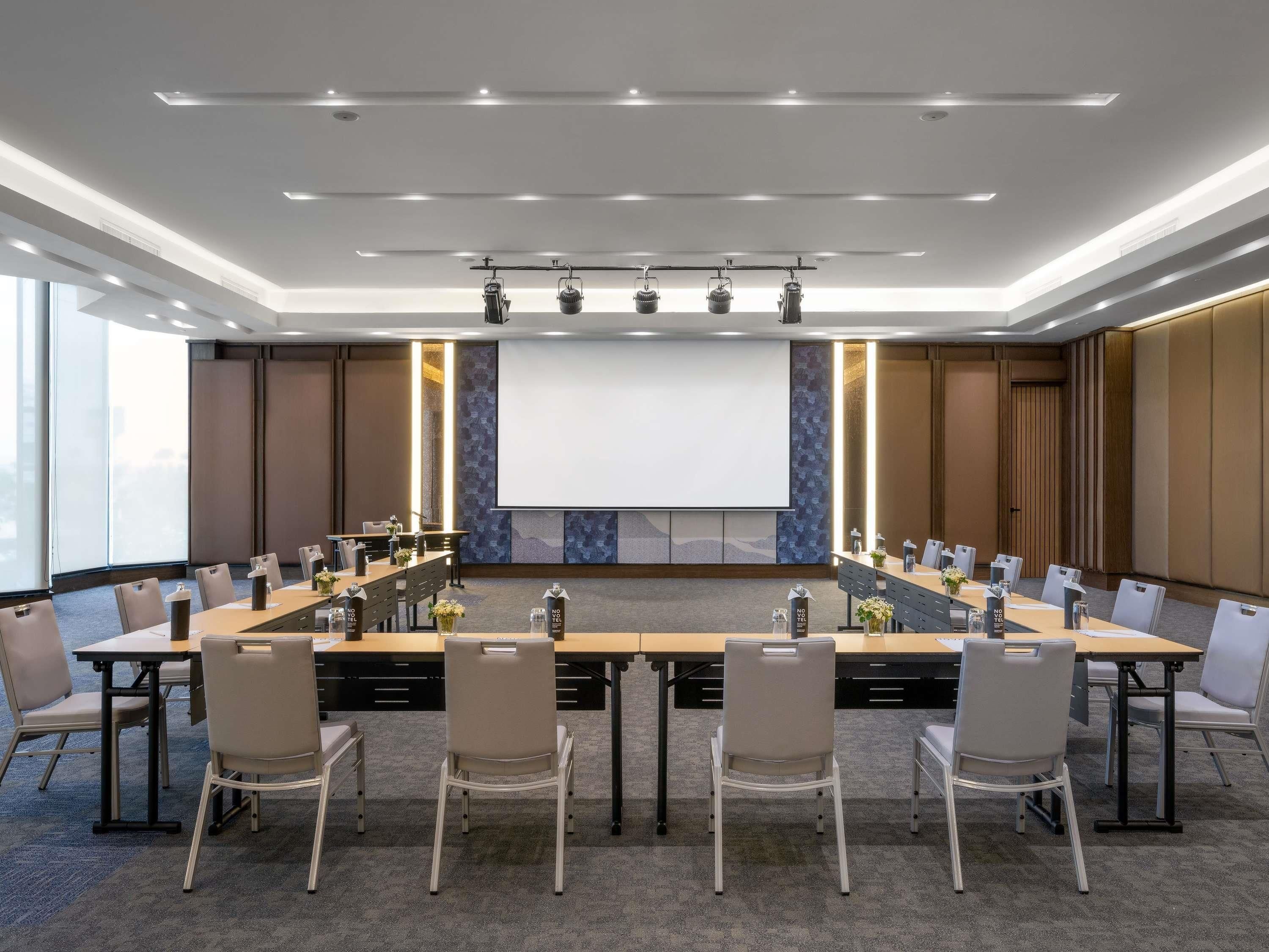 Un salón de conferencias con una larga mesa, sillas, una pantalla de proyector y un amplio ventanal.