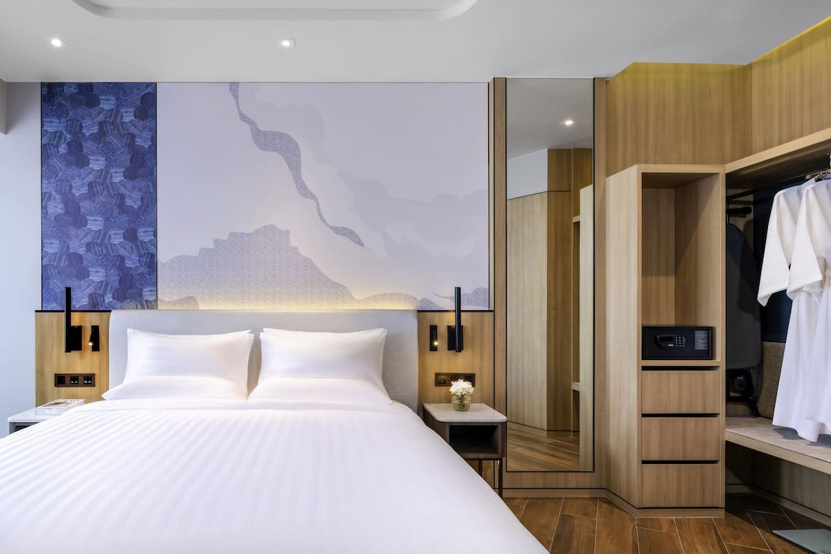 Una habitación de hotel moderna con una cama grande, un armario de madera y una pared decorada con arte abstracto.