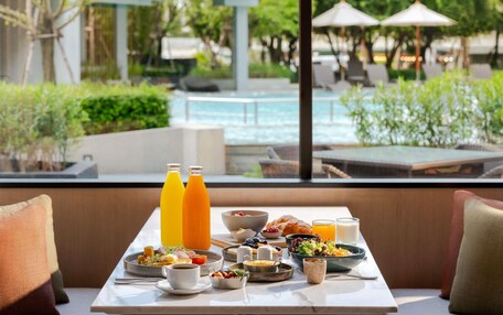 A breakfast table with a variety of dishes, including eggs, toast, and fruit, set against a backdrop of a pool and greenery.