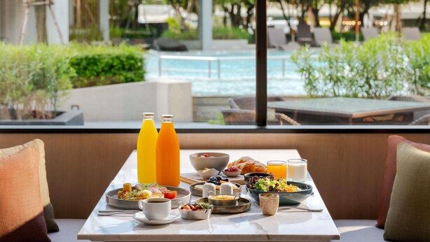 Mesa de café da manhã com diversos pratos, incluindo ovos, torradas e frutas, ao fundo uma piscina e vegetação.