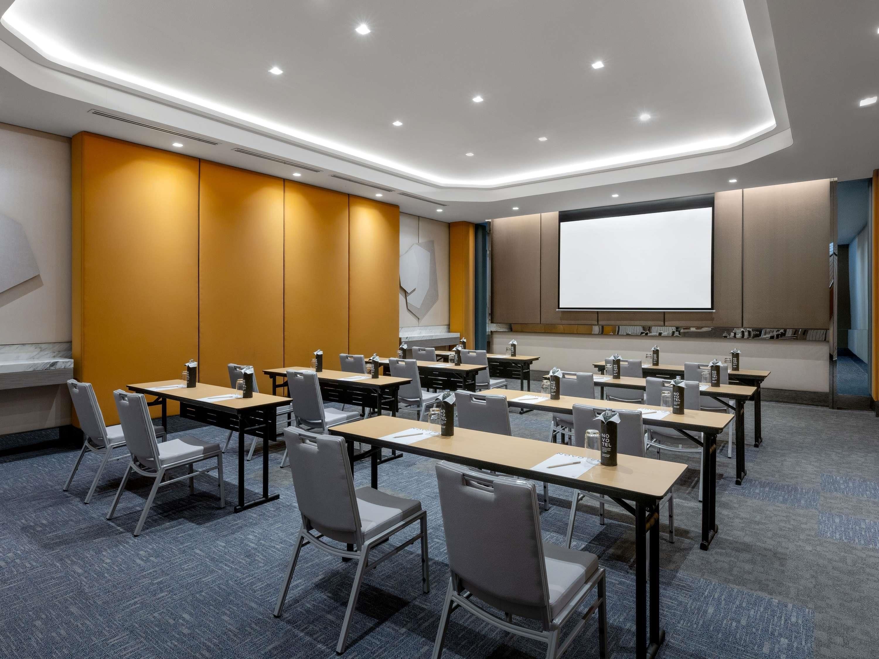 A conference room with tables, chairs, a projector screen, and a carpeted floor.