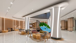 Um hall amplo com design moderno, apresentando uma área de estar central com sofás e cadeiras, uma grande obra de arte na parede e um teto alto com iluminação embutida.